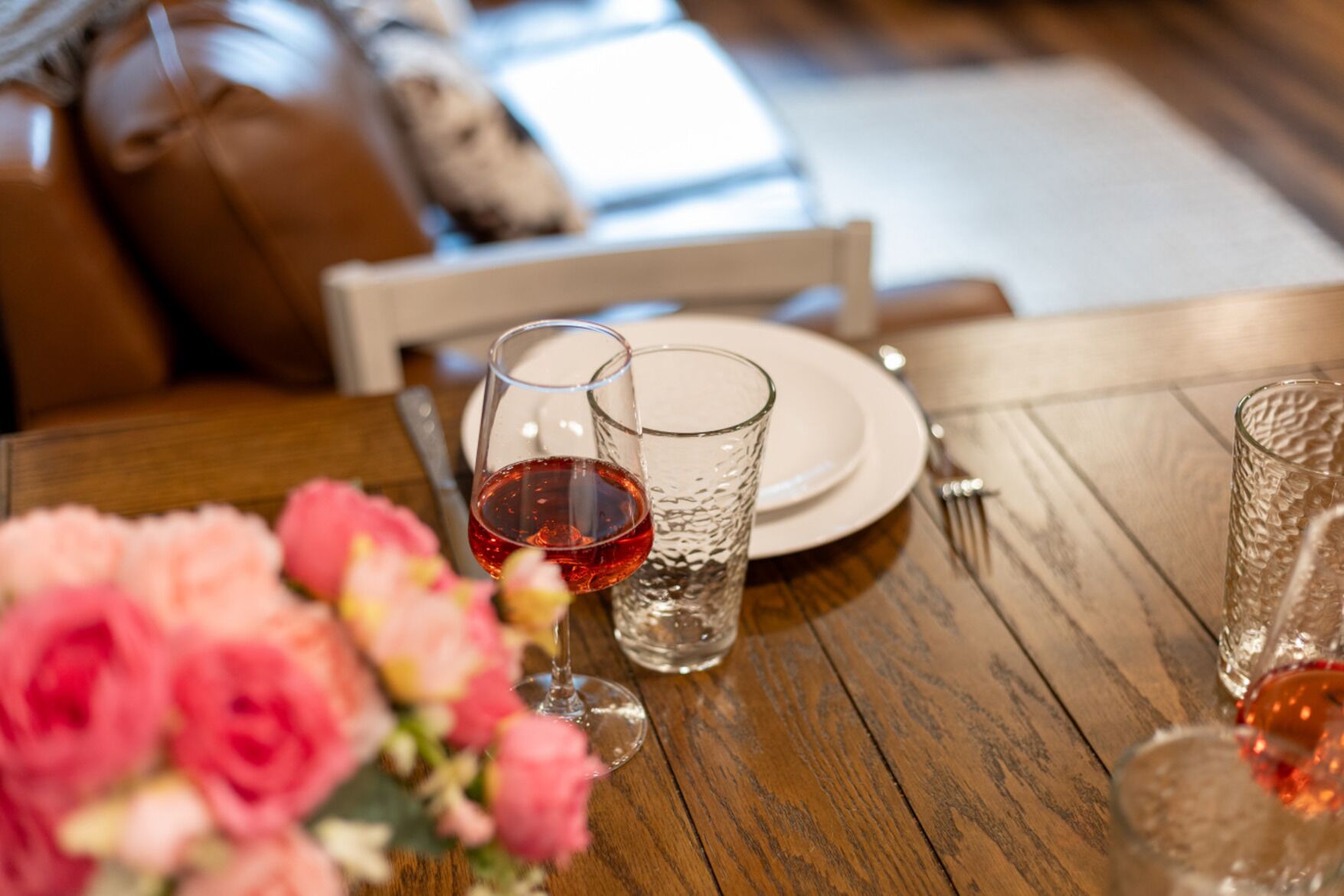 Une table de salle à manger en bois, avec une assiette, un verre de vin rouge et un verre d’eau.