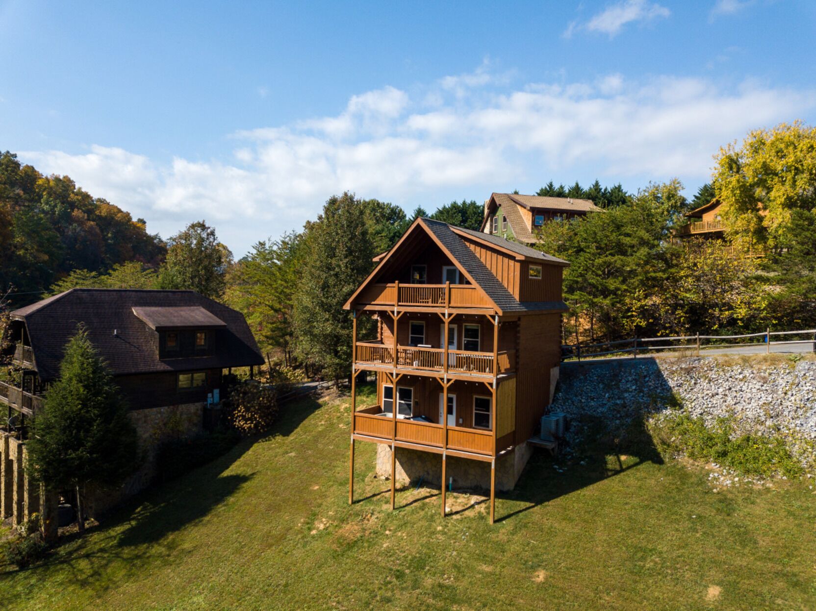 Une cabane en bois à deux étages, dotée d’un balcon, entourée d’arbres et d’un mur de pierres.