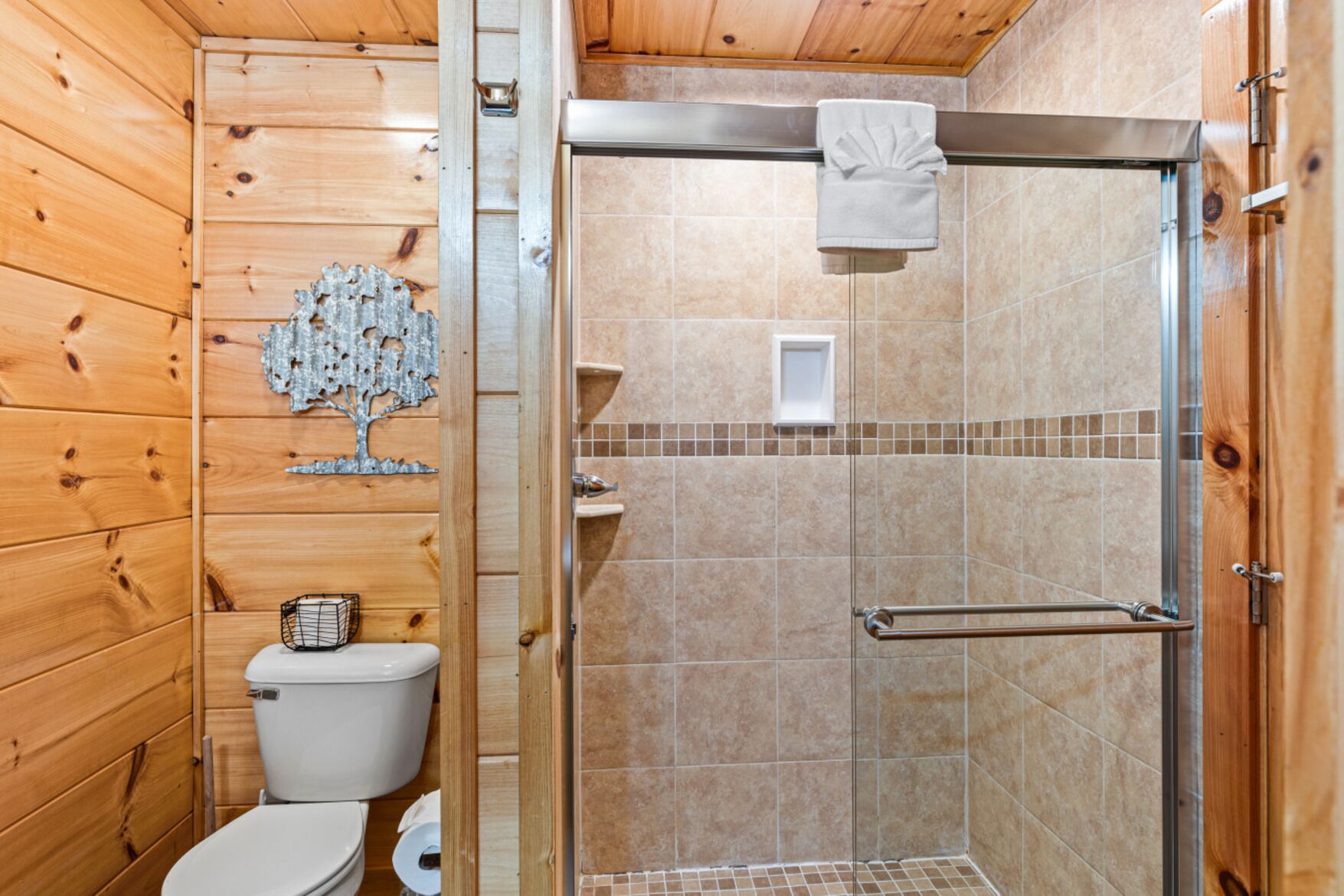A wooden cabin bathroom with a shower, toilet, and a decorative tree wall.