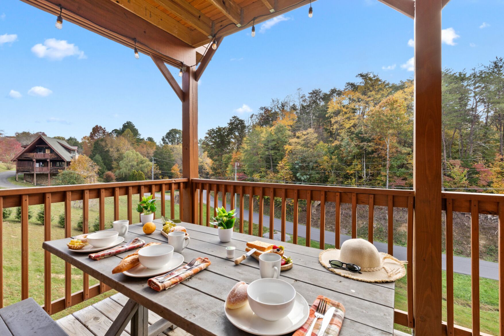 A wooden deck with a table set for breakfast, overlooking a forested area with autumn foliage.