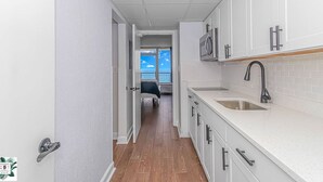 A narrow hallway leading to a kitchen with white cabinets, a stainless steel sink, and a microwave. - Direct Oceanfront Two Bedroom Condo (Myrtle Beach)