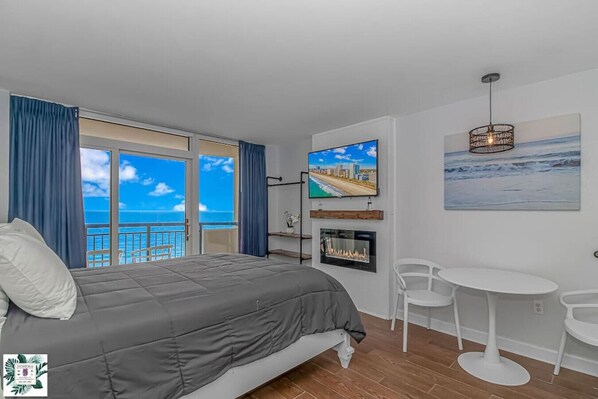 A bedroom with a bed, a TV, a fireplace, and a balcony with a view of the ocean. - Direct Oceanfront Two Bedroom Condo (Myrtle Beach)