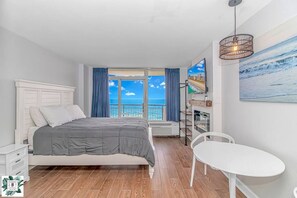 A bedroom with a bed, a white table, and a view of the sea. - Direct Oceanfront Two Bedroom Condo (Myrtle Beach)