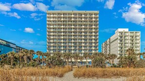 A multi-story hotel with a central courtyard, surrounded by palm trees and a sandy path. - Direct Oceanfront Two Bedroom Condo (Myrtle Beach)