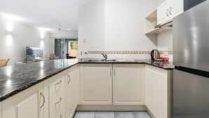A modern kitchen with white cabinets, a black countertop, and a stainless steel refrigerator. - 2 Bedroom Dual Key Pool View Apartment at Alassio (Palm Cove)