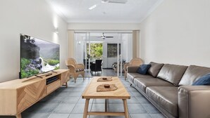 A modern living room with a flat-screen TV, wooden furniture, a leather sofa, and a dining area with chairs and a table. - 2 Bedroom Dual Key Pool View Apartment at Alassio (Palm Cove)