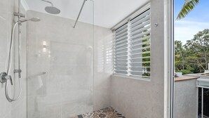 Une salle de bain moderne avec une douche, des murs carrelés et une fenêtre équipée de stores.