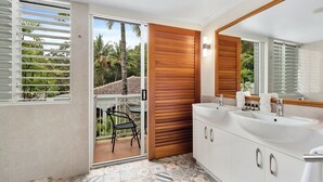 Une salle de bain avec deux lavabos, un grand miroir et une porte-fenêtre coulissante donnant sur un balcon équipé d’une chaise.