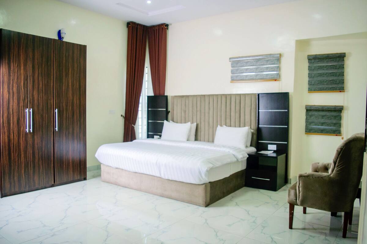 A bedroom with a large bed, a wardrobe, a chair, and artwork on the walls.