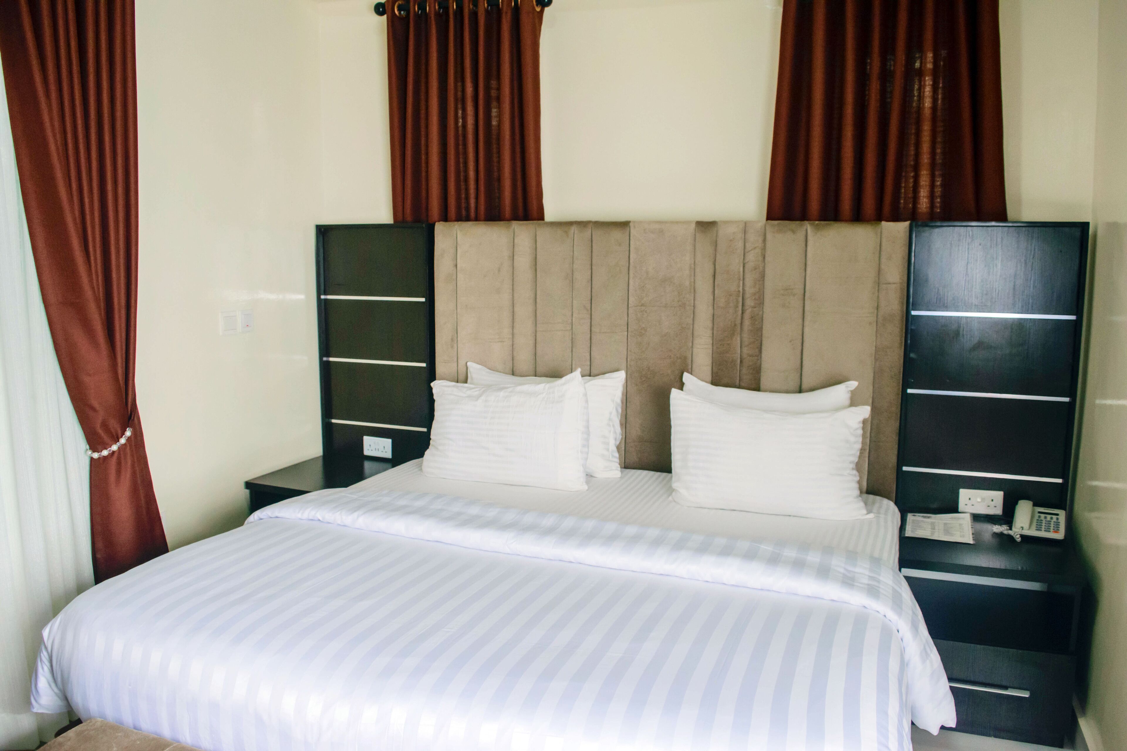 A hotel room with a bed, two nightstands, a telephone, and curtains.