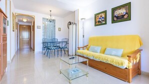 A living room with a yellow sofa, a glass coffee table, and a dining area with a glass table and chairs. - Torre del Rey by Interhome (Oropesa del Mar)