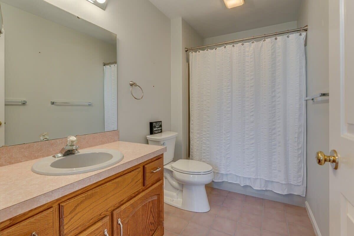 A bathroom with a sink, mirror, toilet, and shower curtain.