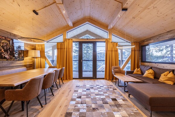 A spacious room with a wooden ceiling, a large window, a checkered floor, a sofa, a table, and chairs.