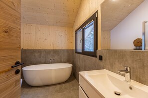 Ein modernes Badezimmer mit freistehender Badewanne, großzügigem Waschbecken und einem Fenster für natürliches Licht.