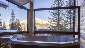 Une cabane en bois dotée d’une grande fenêtre, d’une terrasse en bois et d’un bain à remous.