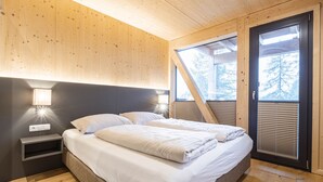 Ein Schlafzimmer mit Holzboden, einem Bett mit weißer Bettwäsche, einem Nachttisch mit Lampe und einem Fenster mit Jalousien.