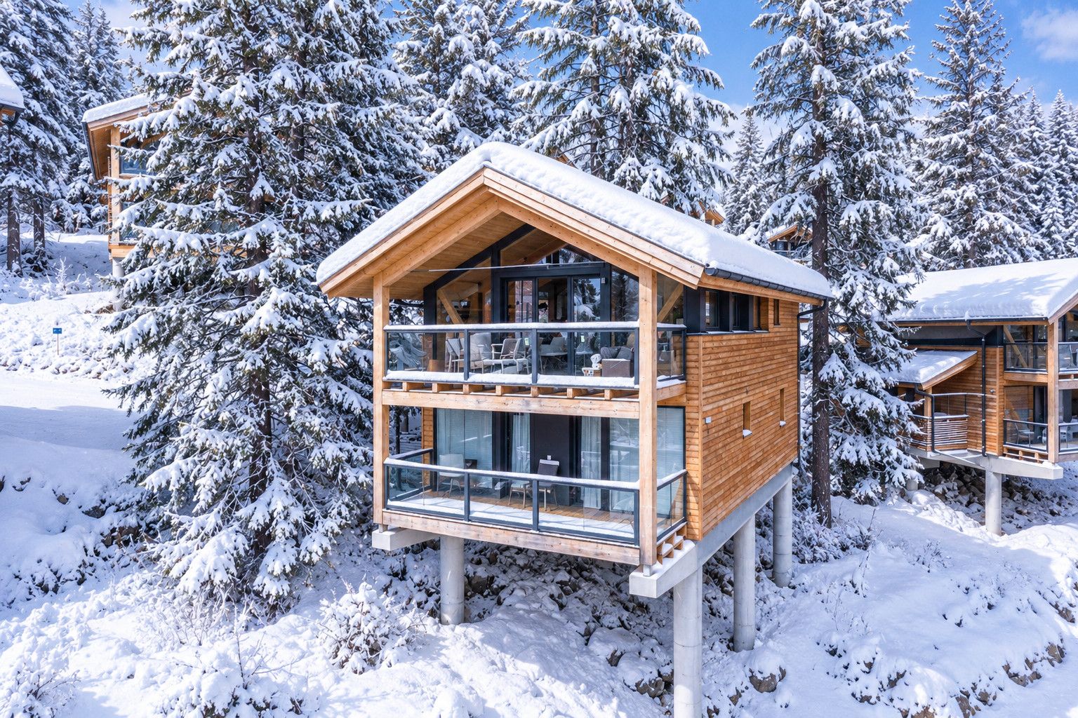 Une cabane en bois dotée d’un balcon en verre, entourée d’arbres couverts de neige.
