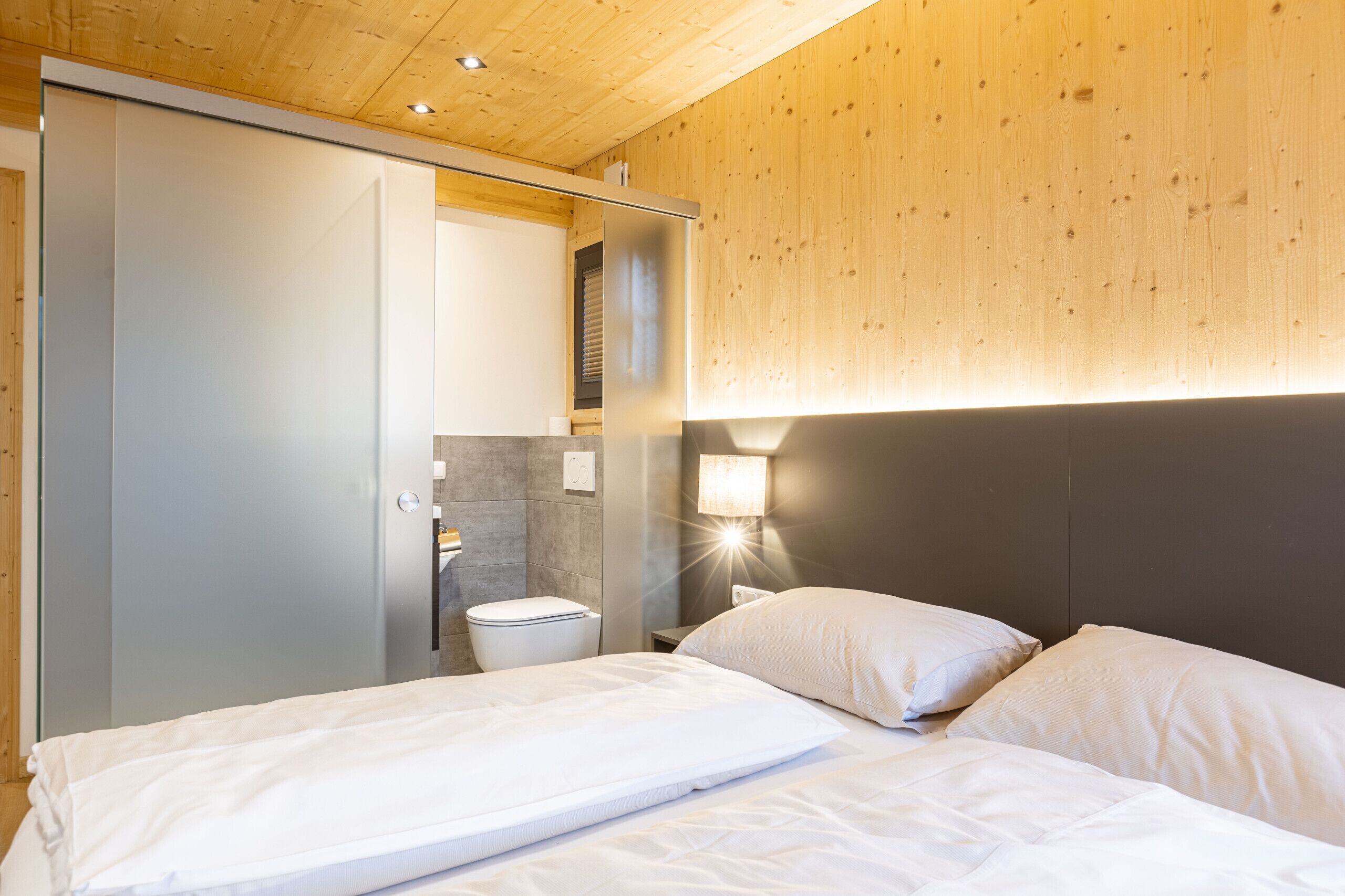 Une chambre à coucher avec un lit, une table de chevet, une lampe fixée au mur et un plafond en bois.