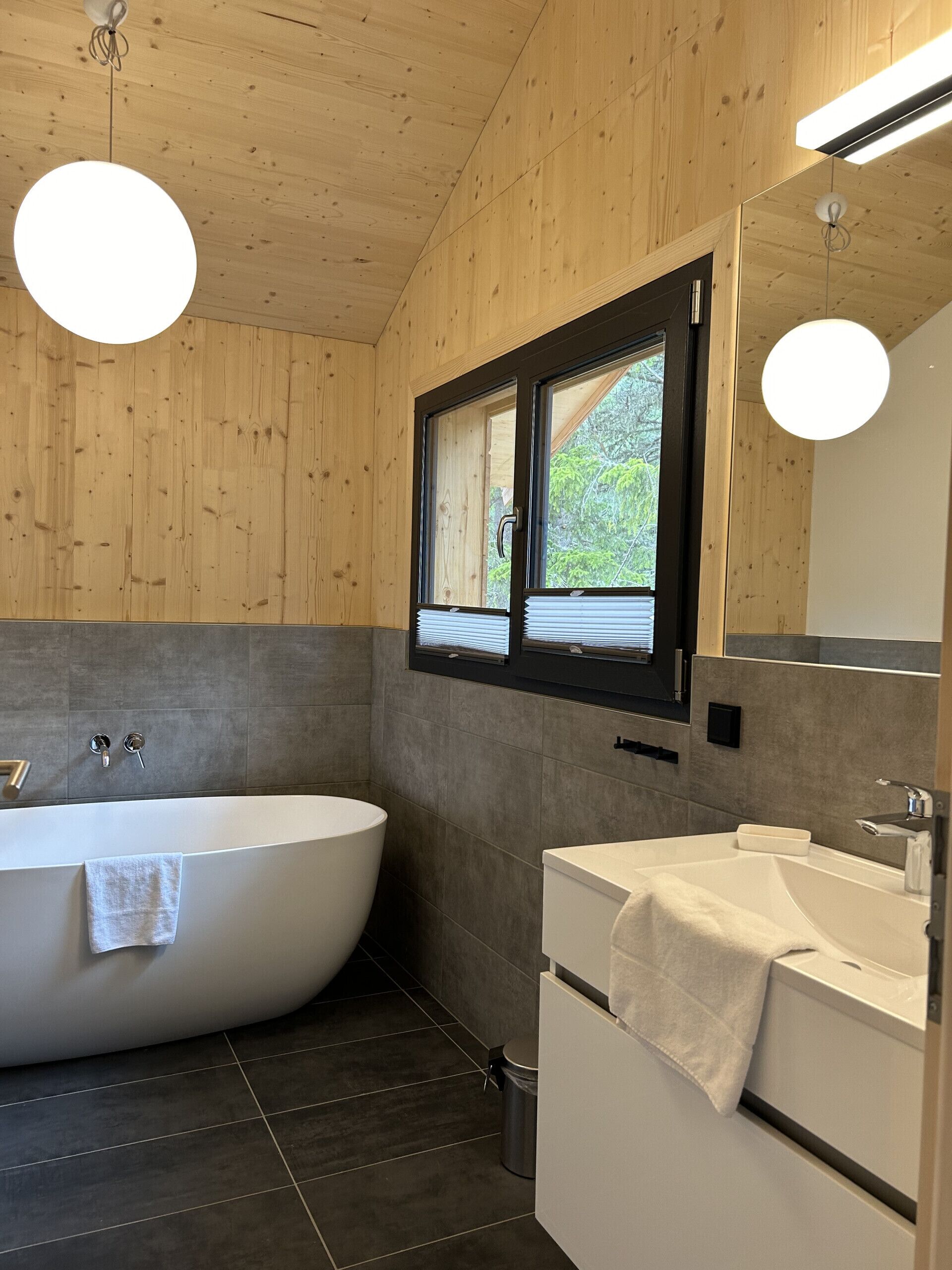 Un baño moderno con una bañera independiente, un lavabo y una ventana con persianas.