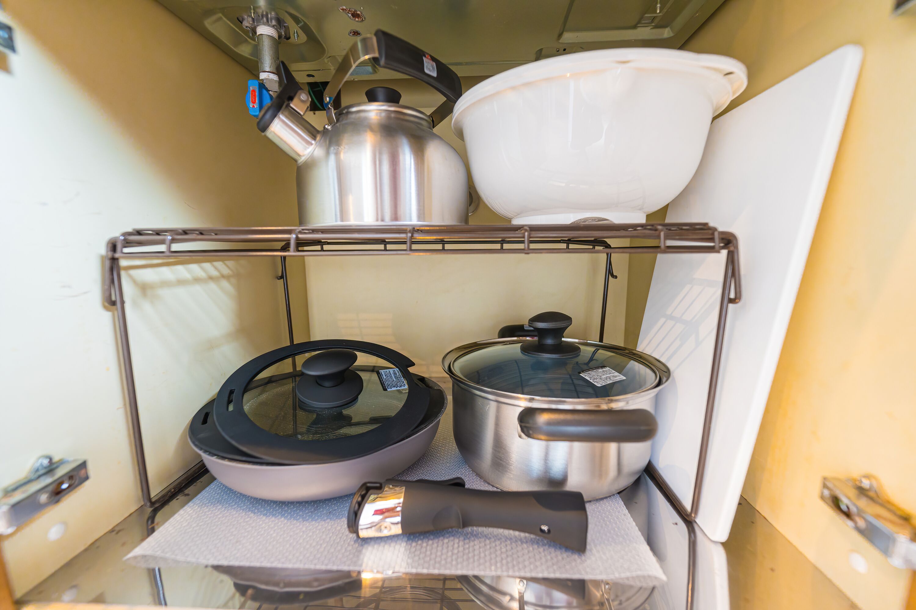 Une cuisine équipée d’une bouilloire en acier inoxydable, d’une casserole, d’une poêle et d’une planche à découper posée sur un étagère.