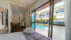 Habitación de hotel con una cama grande, un escritorio y vistas a una piscina y edificios.