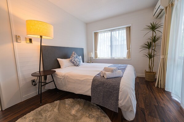 A neatly arranged bedroom with a bed, bedside lamp, and a window with curtains.