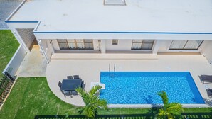Una casa moderna con piscina rectangular, un porche cubierto con mobiliario exterior y un césped bien cuidado.