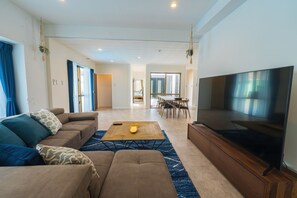 A modern living room with a sofa, coffee table, and TV. There is a dining area with chairs and a table in the background.