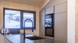 Een keuken met een granieten aanrechtblad, roestvrijstalen apparatuur en een raam met uitzicht op een besneeerd landschap.