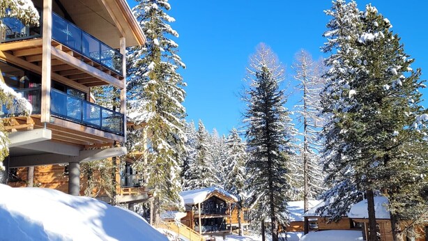 Un bâtiment moderne abritant un centre de ski, doté de nombreux balcons et d’une façade en bois, et entouré d’arbres couverts de neige.