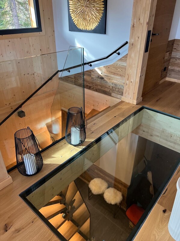 A modern interior with a glass staircase, wooden flooring, and a unique wall art piece.