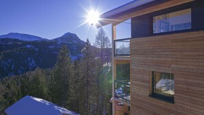 Una cabaña de madera moderna con balcón que da a un paisaje montañoso nevado.