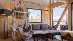 Una habitación acogedora con una hamaca, un sofá, una mesa y vistas a montañas nevadas a través de amplias ventanas.