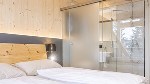 Ein modernes Schlafzimmer mit einem Holzkopfteil, einer Duschkabine aus Glas und einem Nachttisch mit Lampe.