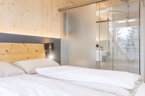 Une chambre à coucher moderne avec une tête de lit en bois, une cabine de douche en verre et une table de chevet avec une lampe.