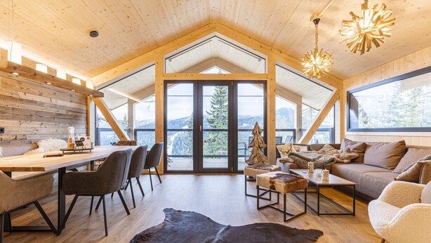 Un vaste espace de vie doté d’un haut plafond, de poutres en bois, d’une grande fenêtre et d’un coin repas avec des chaises et une table.