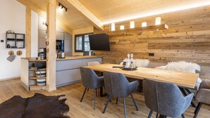 Une cuisine moderne avec des meubles en bois, un coin repas avec une table en bois et des chaises grises, et un coin salon confortable agrémenté d’un tapis en fourrure.