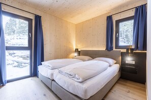 Un dormitorio de cabaña de madera con dos camas, una mesita de noche y una ventana con cortinas.