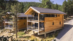 Eine Holzhütte mit Balkon und überdachter Terrasse, umgeben von Bäumen.