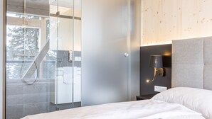 Ein modernes Hotelzimmer mit Duschkabine aus Glas, einem Bett mit weißer Bettwäsche und einer Wandlampe.
