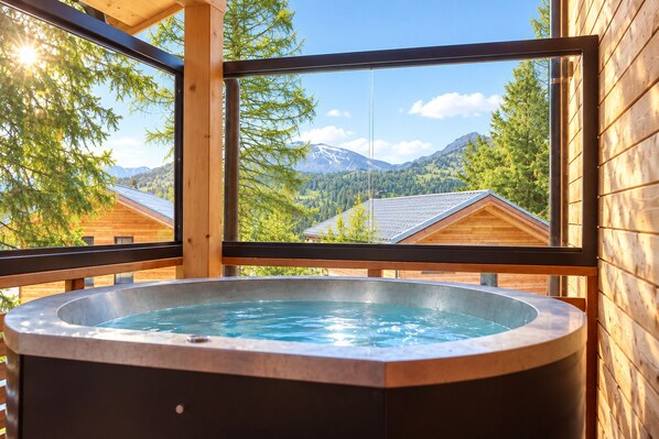 A hot tub with a mountain view, wooden cabin walls, and a clear sky.