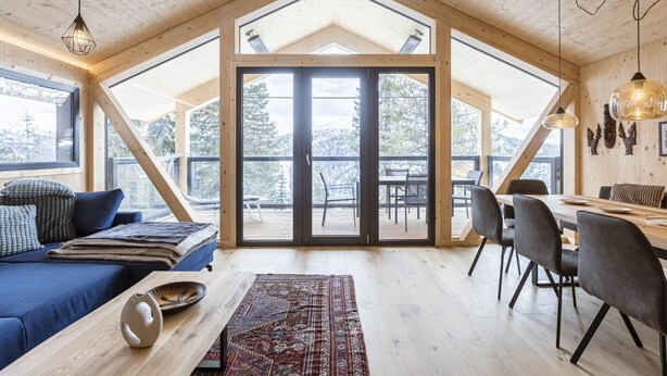 Ein geräumiges Zimmer mit hoher Decke, Holzbalken, einer großen Schiebeglas-Zuwegung zu einer Außenterrasse, einem Essbereich mit Tisch und Stühlen und einer gemütlichen Sitzecke mit Sofa und Kissen.