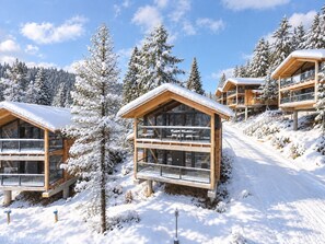 Un edificio de estilo chalé con balcones de madera, rodeado de árboles cubiertos de nieve y un cielo despejado.