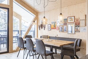 Un espace de salle à manger moderne avec une table en bois, des chaises à revêtement gris et des luminaires suspendus.