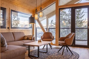 A cozy room with a wooden ceiling, large windows, a sofa, a table, and two chairs.