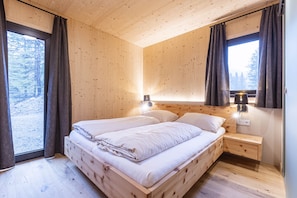 A wooden cabin bedroom with a bed, bedside tables, and a window with curtains.
