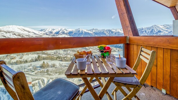 Een houten terras met een tafel en stoelen, met uitzicht op een besneeerd berglandschap.