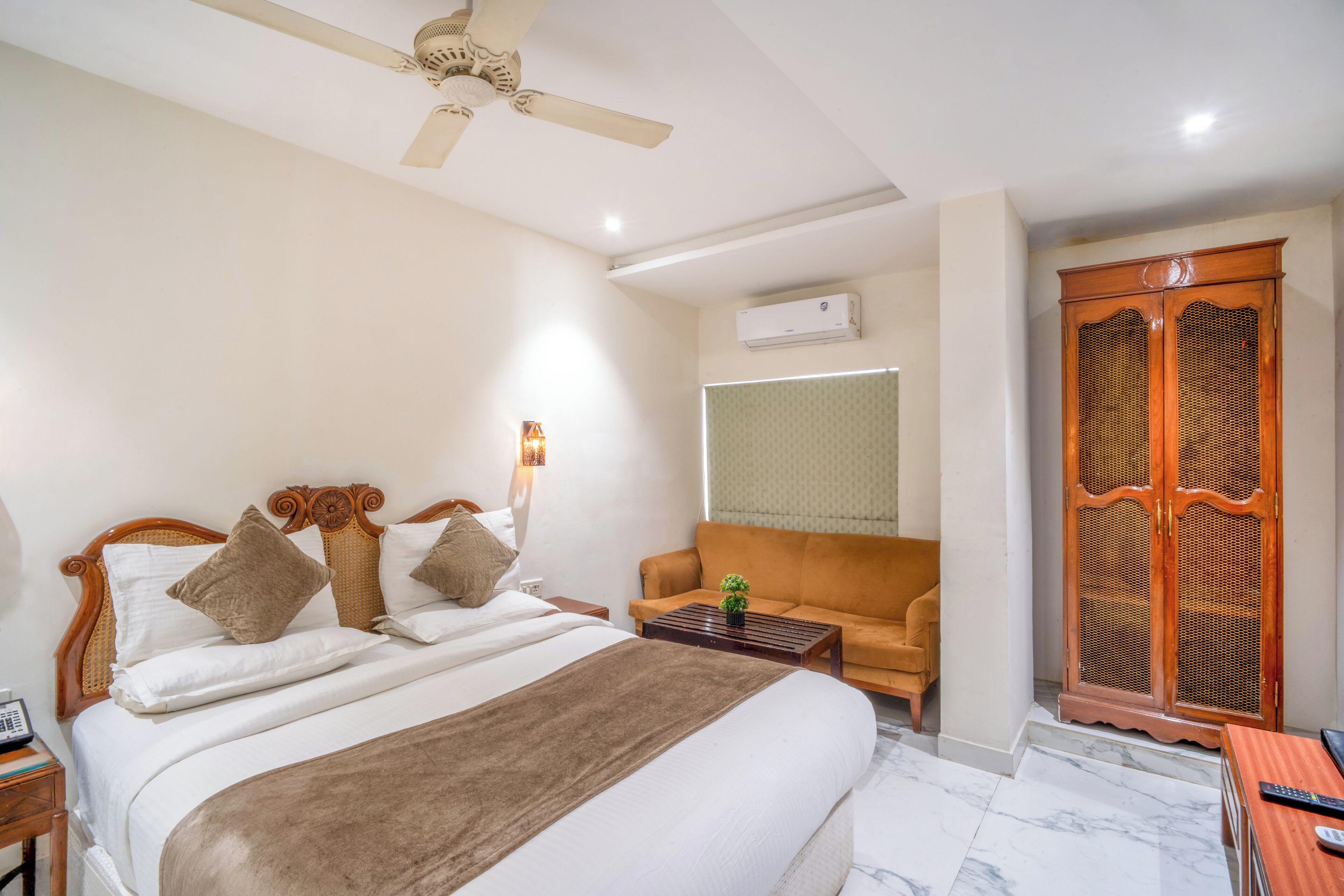 Una habitación de hotel con una cama, un sofá, un armario de madera y un ventilador de techo.