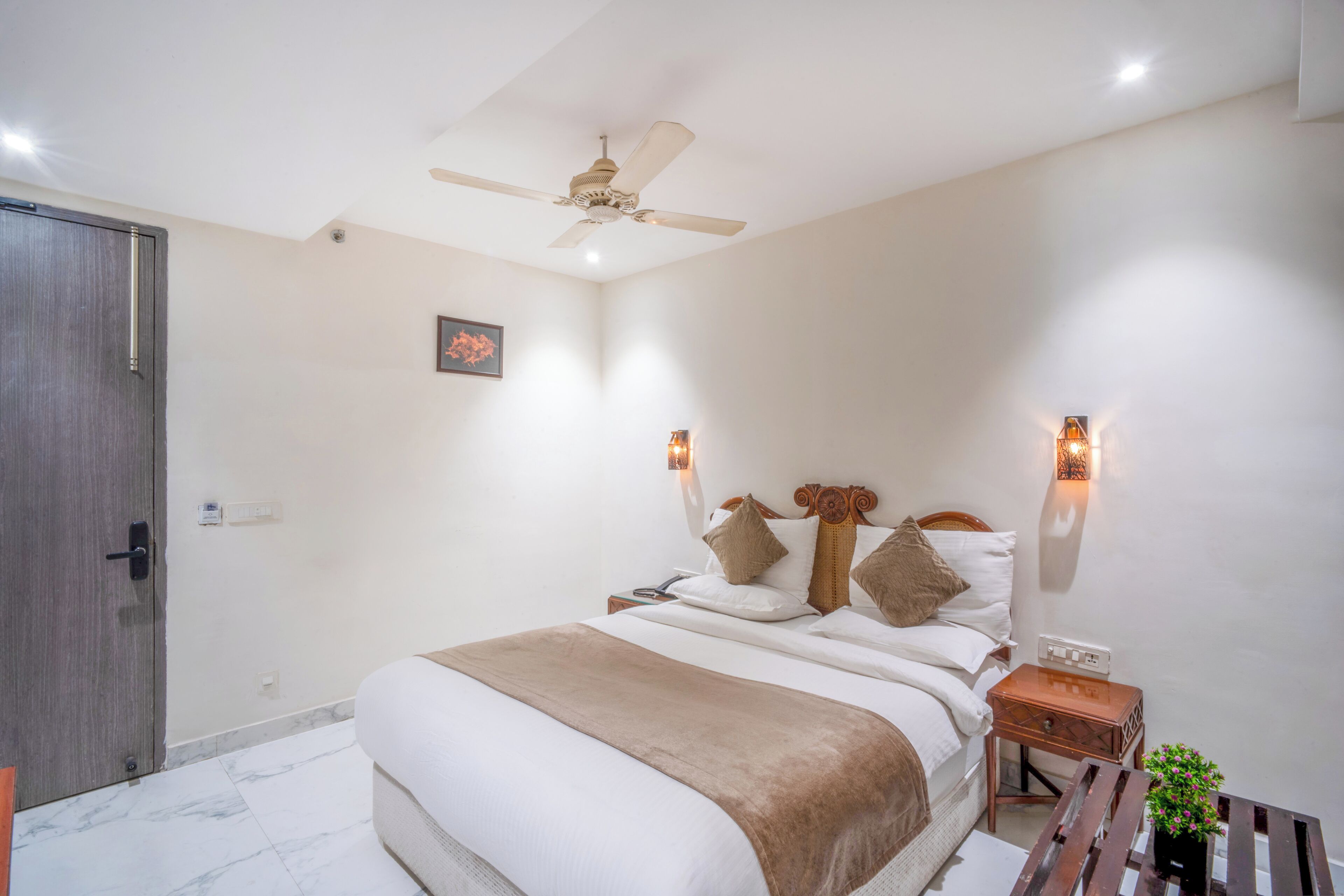 A bedroom with a bed, bedside tables, a nightstand, a ceiling fan, and wall-mounted lights.