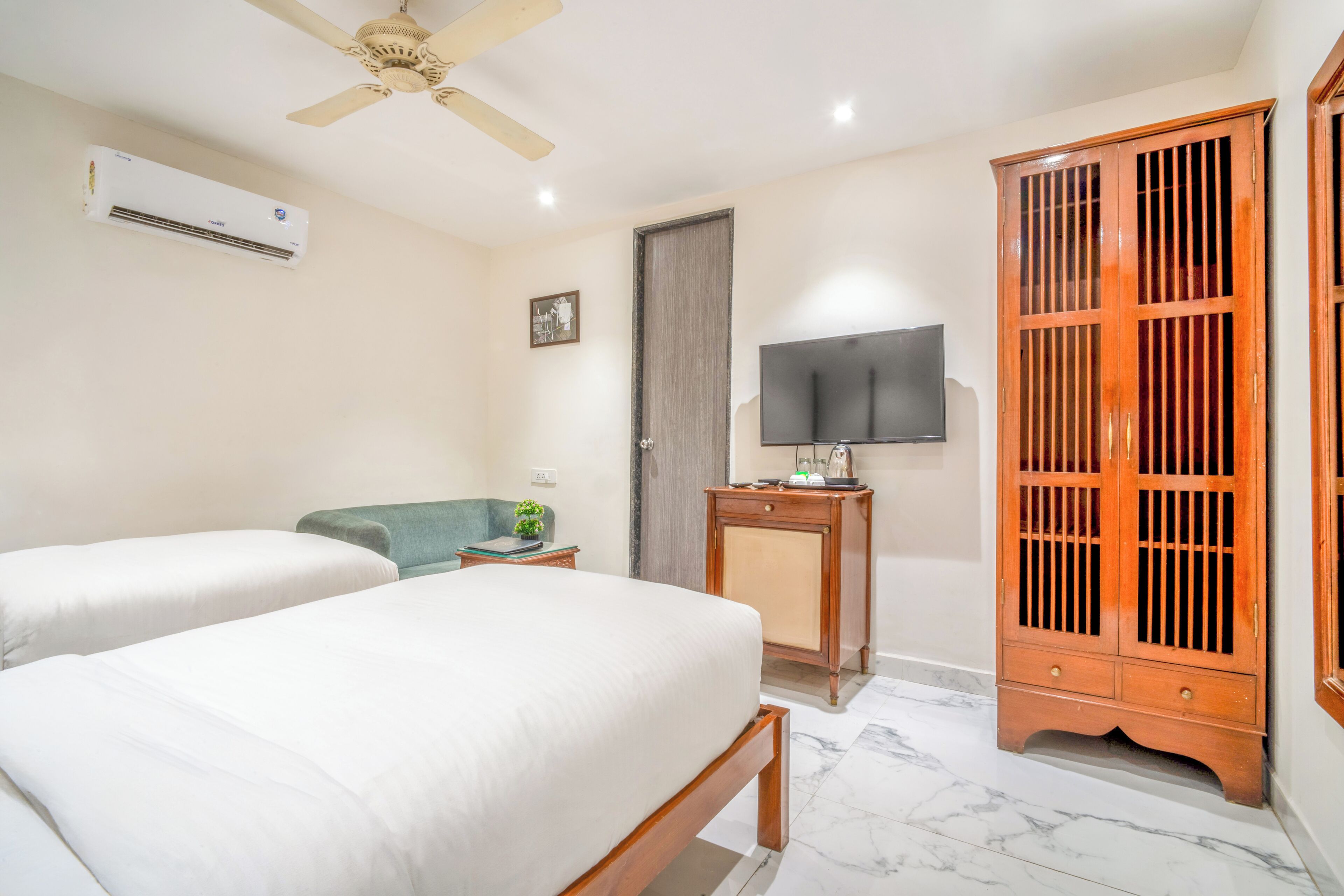 A hotel room with two beds, a television, a wardrobe, and an air conditioning unit.